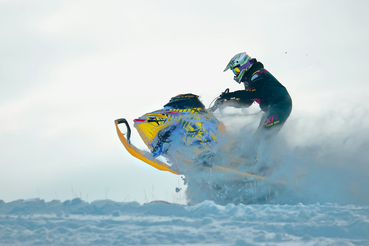 Snowmobile launching off a snow ridge throwing powder